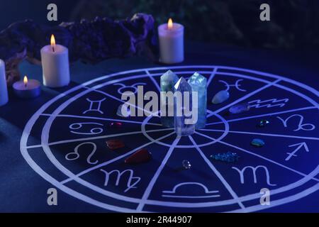 Pierres naturelles pour les signes du zodiaque, carte d'astrologie dessinée et bougies allumées sur table bleu foncé Banque D'Images