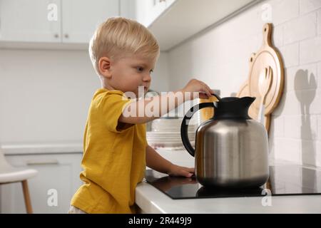 Curieux petit garçon jouant avec bouilloire sur cuisinière électrique dans la cuisine Banque D'Images