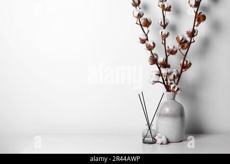 Diffuseur en roseau et vase avec branches en coton sur table sur fond blanc. Espace pour le texte Banque D'Images
