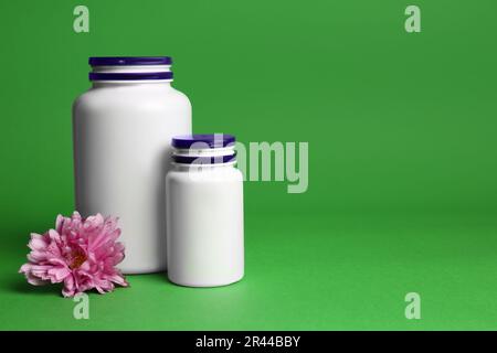 Bouteilles de médicaments en plastique et fleur rose sur fond vert, espace pour le texte. Médicament Banque D'Images