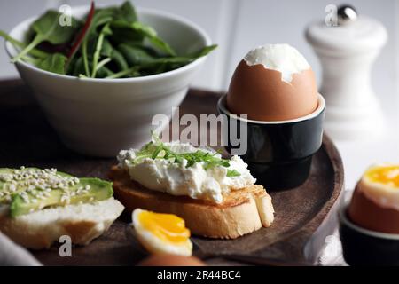 Œuf frais et doux dans une tasse et sandwichs sur un plateau en bois Banque D'Images