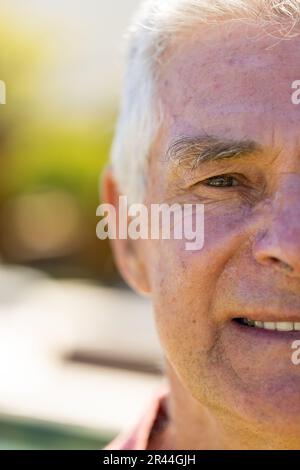 Demi portrait d'un homme caucasien âgé heureux regardant l'appareil photo et souriant dans un jardin ensoleillé Banque D'Images