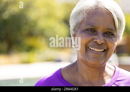 Portrait d'une heureuse femme biraciale senior regardant l'appareil photo et souriant dans un jardin ensoleillé, espace copie Banque D'Images