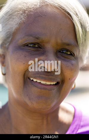 Portrait d'une heureuse femme biraciale senior regardant l'appareil photo et souriant dans un jardin ensoleillé Banque D'Images