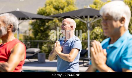 Heureux divers hommes senior amis pratiquant le yoga et méditant debout dans le jardin ensoleillé Banque D'Images