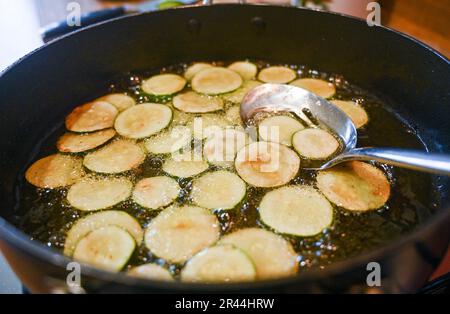 Friture ou brunissage de tranches de courgettes ou de courgettes dans de l'huile de tournesol prête à l'emploi dans un plat de pâtes italien Banque D'Images