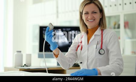 Femme souriante médecin tenant la sonde à ultrasons dans ses mains en clinique Banque D'Images