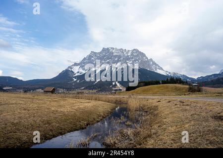 Une vue panoramique d'une crique qui coule à travers un champ herbeux contre la montagne Zugspitze en Allemagne Banque D'Images