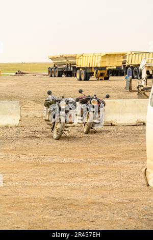 Deux motos garées dans un champ de terre avec deux camions en arrière-plan, offrant une scène pittoresque de terrain rural Banque D'Images