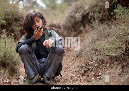 Un enfant est assis au milieu du sentier, captivé, comme ils observent la boussole, démêlant les mystères de la navigation et de la direction. Banque D'Images