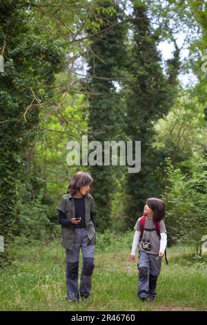 Deux frères et sœurs se promènent dans une clairière boisée, engagés dans la conversation, enveloppée par la tranquillité de l'étreinte de la nature. Banque D'Images