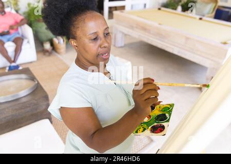 Focalisé bonne femme afro-américaine senior tenant la palette et la toile de peinture sur le chevalet Banque D'Images