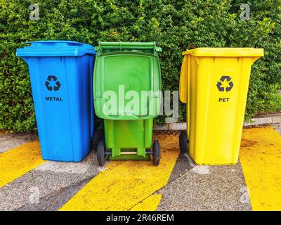 Une rangée de trois poubelles extérieures aux couleurs vives alignées sur un trottoir. Banque D'Images