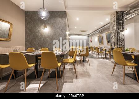 Hall d'un restaurant avec tables à manger en bois et chaises jaunes, miroirs avec cadres dorés sur les murs et sols carrelés Banque D'Images