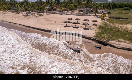 Petit bateau de pêche en contrebas enterré dans le sable sur une côte de la mer des Caraïbes, découvert par des vagues, avec des maisons et des huttes à l'arrière Banque D'Images