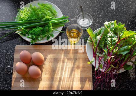 Salade de jeunes feuilles de betteraves. Légumes frais et légumes verts, œufs de poulet bouillis sur la table à côté de la planche à découper pour préparer la salade de printemps. Banque D'Images