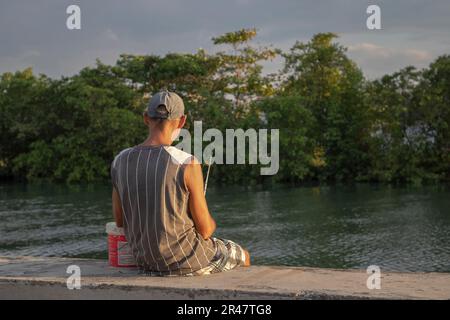 Un pêcheur mâle se tient sur la rive de la rivière San Juan de Matanzas à Cuba, portant fièrement une canne à pêche Banque D'Images