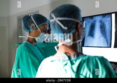 Divers chirurgiens masculins et féminins regardant les rayons X dans le bloc opératoire avant la chirurgie Banque D'Images