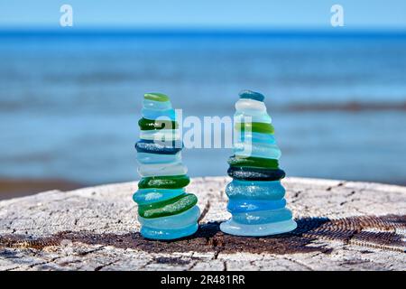 Deux pyramides équilibrées de la mer humide, la bouteille de verre poli sur une surface de bois abîmée contre la mer Banque D'Images