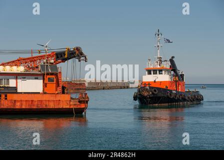 Héraklion, Crète, Grèce. 2023. Remorqueur approchant une grande barge de grue en mer avec une grue montée sur le pont le long du port. Banque D'Images