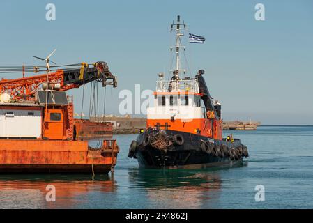 Héraklion, Crète, Grèce. 2023. Remorqueur approchant une grande barge de grue en mer avec une grue montée sur le pont le long du port. Banque D'Images