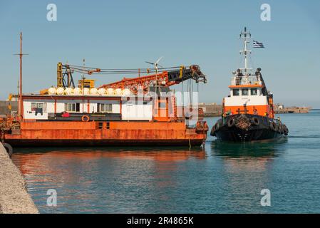 Héraklion, Crète, Grèce. 2023. Remorqueur approchant une grande barge de grue en mer avec une grue montée sur le pont le long du port. Banque D'Images