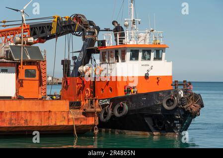 Héraklion, Crète, Grèce. 2023. Remorqueur venant le long d'une grande barge de grue en mer avec une grue montée sur le pont le long du port. Banque D'Images