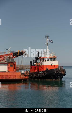 Héraklion, Crète, Grèce. 2023. Remorqueur venant le long d'une grande barge de grue en mer avec une grue montée sur le pont le long du port. Banque D'Images