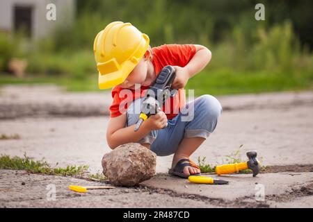 Petit garçon avec des outils de jouet à l'extérieur. Impliquer l'enfant dans le travail Banque D'Images