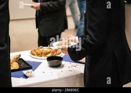 Les personnes en costume se servent au buffet et mangent de délicieux plats lors d'un événement d'affaires. Il y a des collations et des amuse-gueules. Banque D'Images
