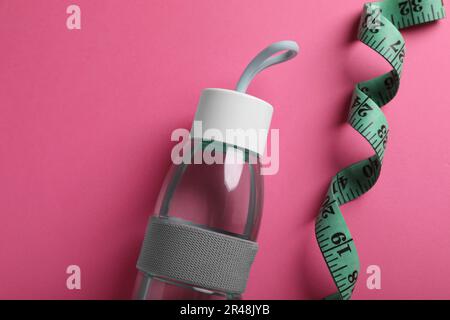 Mètre ruban et bouteille avec eau sur fond rose, plat. Concept de contrôle du poids Banque D'Images