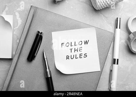 Note sur papier avec phrase Suivez les règles et la papeterie sur table en marbre gris, plat Banque D'Images
