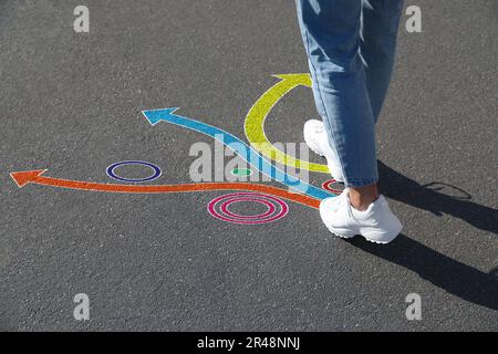 Choix. Femme marchant vers des marques tracées sur la route, gros plan. Flèches colorées pointant dans différentes directions Banque D'Images