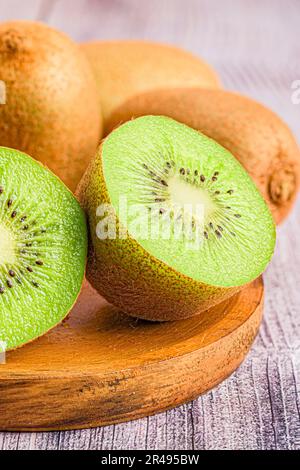 Gros plan d'une plaque en bois avec trois kiwis mûrs, dont l'un coupé en deux moitiés, sur une surface de table Banque D'Images