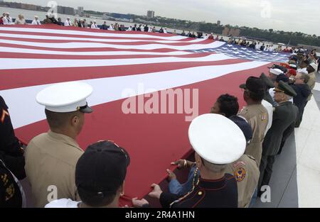 LES marins de la Marine AMÉRICAINE, les Marines et les anciens combattants militaires détiennent un grand drapeau américain pendant le jeu de TAP lors d'une commémoration du jour du souvenir Banque D'Images