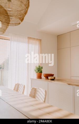 Cette salle à manger moderne est dotée d''un mobilier aux couleurs claires et d''une grande fenêtre avec des stores Banque D'Images