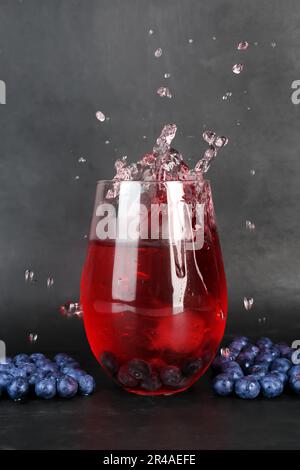 Verre de cidre de myrtille savoureux avec des éclaboussures, un cube de glace et des baies sur fond sombre Banque D'Images