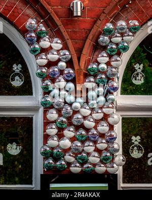 Une sculpture de boules de Noël festive est suspendue à un mur, éclairée par la lumière d'une fenêtre voisine Banque D'Images