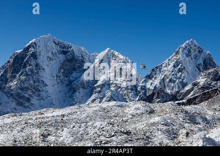 Hélicoptère de sauvetage dans les hautes montagnes de l'Himalaya. Hélicoptère rouge volant entre deux magnifiques sommets enneigés lors d'une journée ensoleillée. Banque D'Images