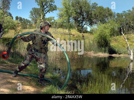 US Navy Utiesman 2nd Class affecté au bataillon de construction mobile navale Two Five (NMCB-25) basé à fort McCoy, Wisconsin, jette un tuyau d'aspiration dans un réservoir local. Banque D'Images