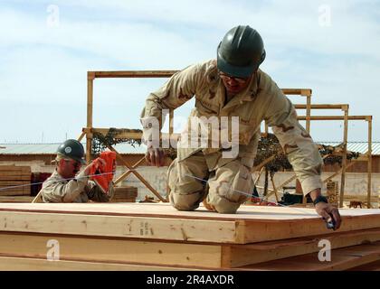 US Navy Builder 1st Class Foreground, marque le contreplaqué pour la coupe, tandis que Utilitesman 2nd Class John Kent exploite un pistolet à ongles pour soutenir les huttes de l'Asie du Sud-Ouest Banque D'Images