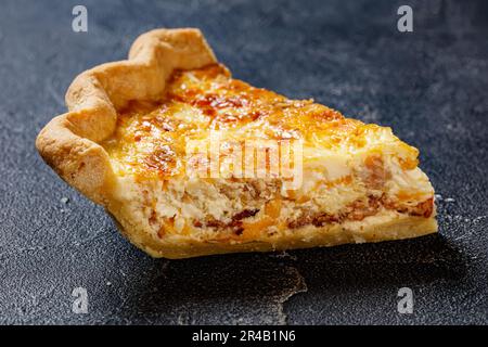 une tranche de quiche de petit déjeuner moelleux avec du fromage et du bacon sur une table en béton, en gros plan Banque D'Images