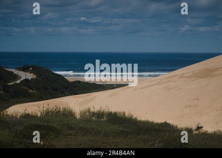 Une personne seule traverse une vaste plage, le soleil se reflétant sur les dunes de sable qui bordent la rive Banque D'Images