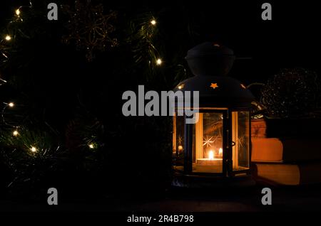 Lanterne blanche avec une bougie allumée. Livres, branche d'arbre de noël et lumières sur fond. Image sombre de nuit. Humeur mystère de Noël Banque D'Images