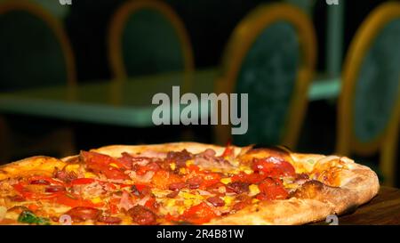 Une pizza savoureuse prête et une table verte avec des chaises dans un café en arrière-plan Banque D'Images