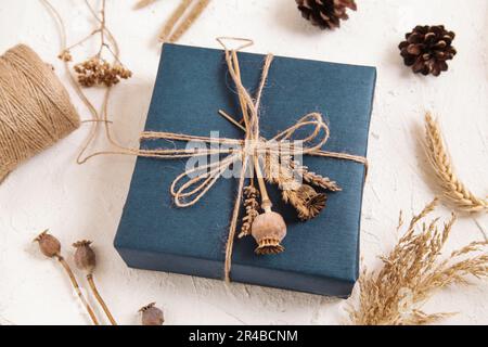 Boîte cadeau faite à la main dans un emballage bleu foncé, têtes de graines de pavot, fleurs séchées. Cadeau pour homme. Fleuriste, herbier artisanal. Couleurs naturelles. vue de dessus. copie s Banque D'Images
