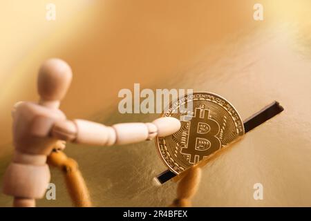 Un homme en bois met une pièce d'or avec un symbole bitcoin dans la fente de la boîte d'or, la banque de piggy. Concept de crypto-monnaie. Mise au point sélective Banque D'Images