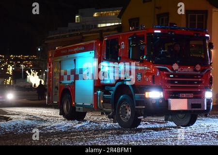 Un camion d'incendie rouge vif descend une rue enneigée d'hiver, ses feux rouges et jaunes clignotent pendant qu'il se déplace Banque D'Images