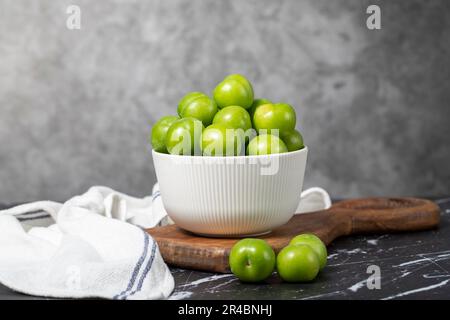 Prune verte dans un bol. Produits agricoles biologiques. Prune douce ou aigre sur fond sombre Banque D'Images