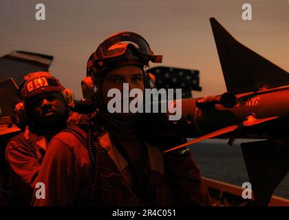 LES militaires DE l'aviation DE LA marine AMÉRICAINE à bord du porte-avions de la classe Nimitz USS Dwight D. Eisenhower (CVN 69) portent un missile d'entraînement Sidewinder pendant les opérations de vol de nuit. Banque D'Images